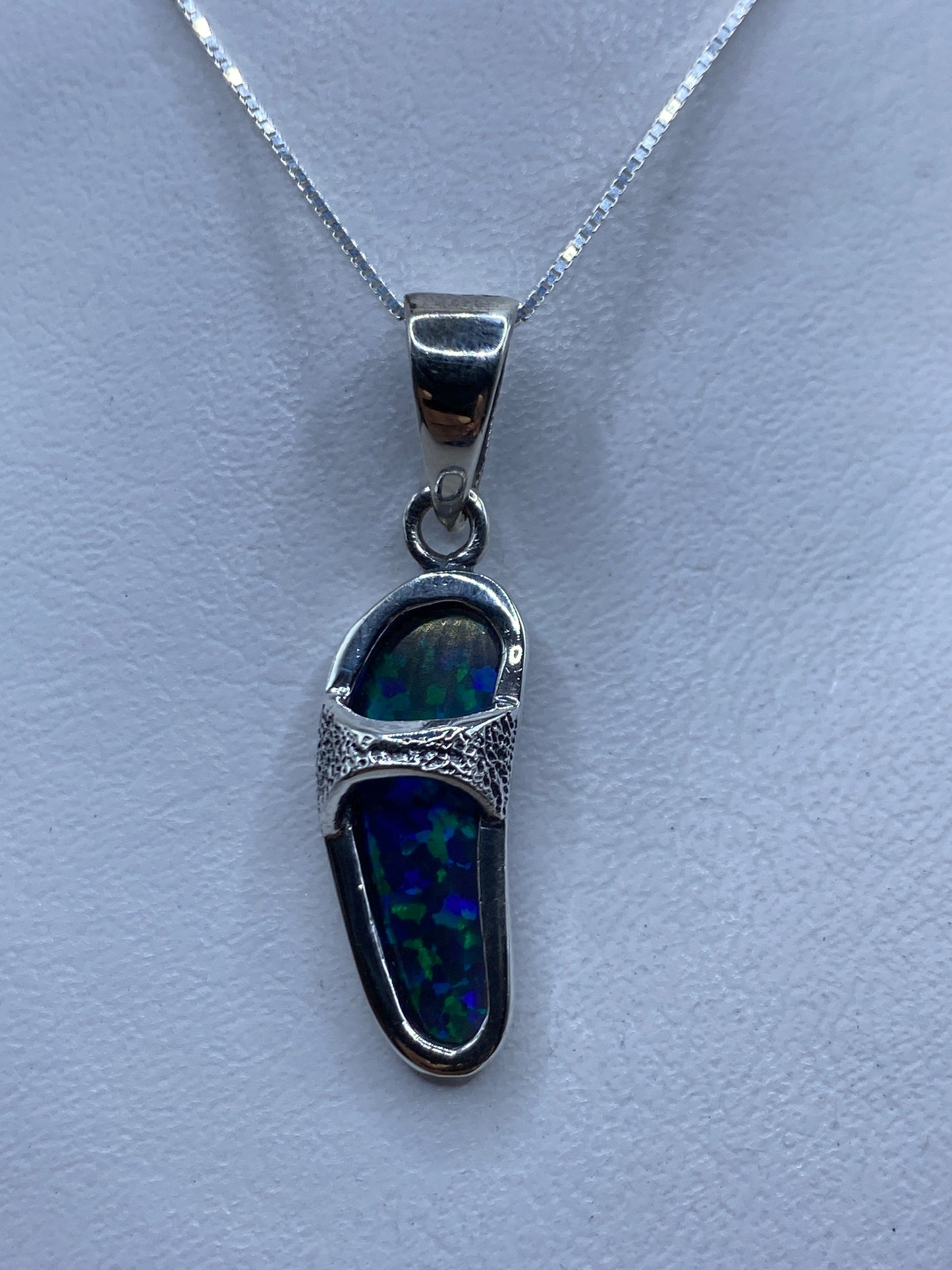 Dije de plata .950 con ópalo de fuego azul, colgado en cadena de plata, sobre fondo blanco