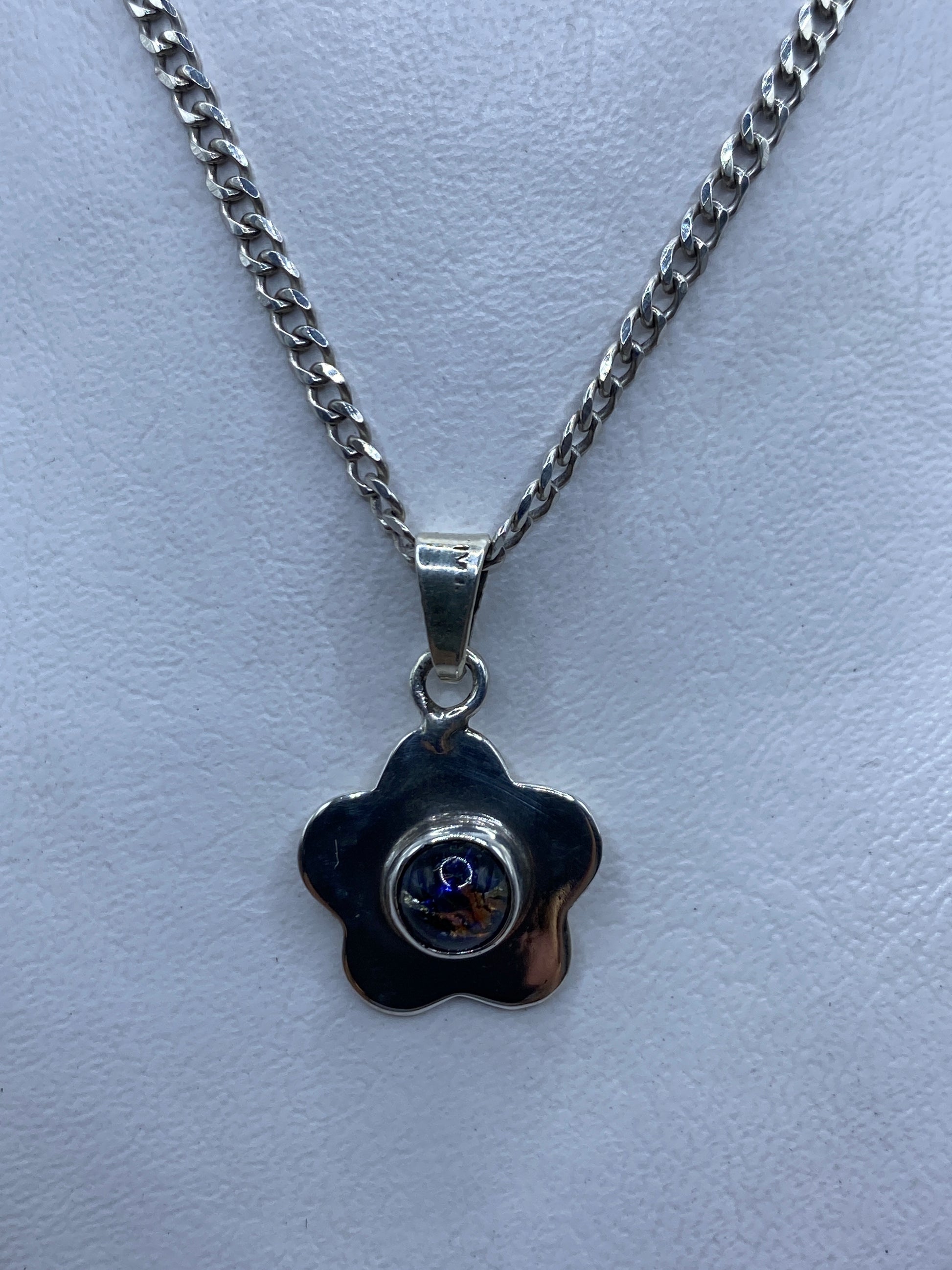 Dije de plata floral con piedras multicolor colgando en cadena de plata, sobre fondo azul