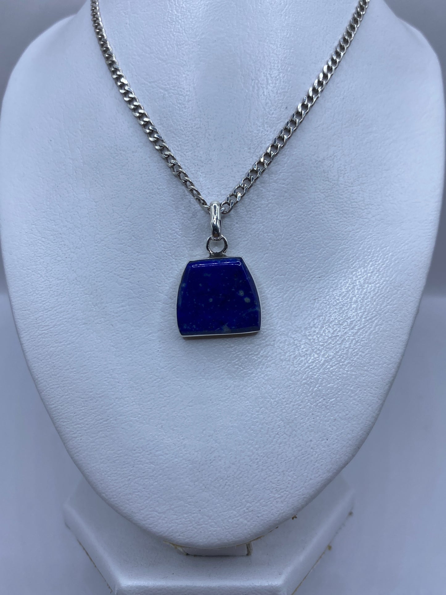 Dije de piedra azul engastada en plata, vista frontal sobre busto blanco