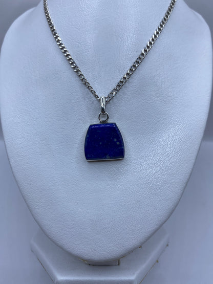 Dije de piedra azul engastada en plata, vista frontal sobre busto blanco