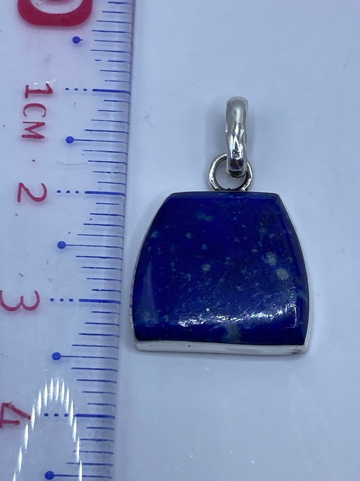Dije de 3.4 cm de largo junto a regla de medición, mostrando el tamaño real