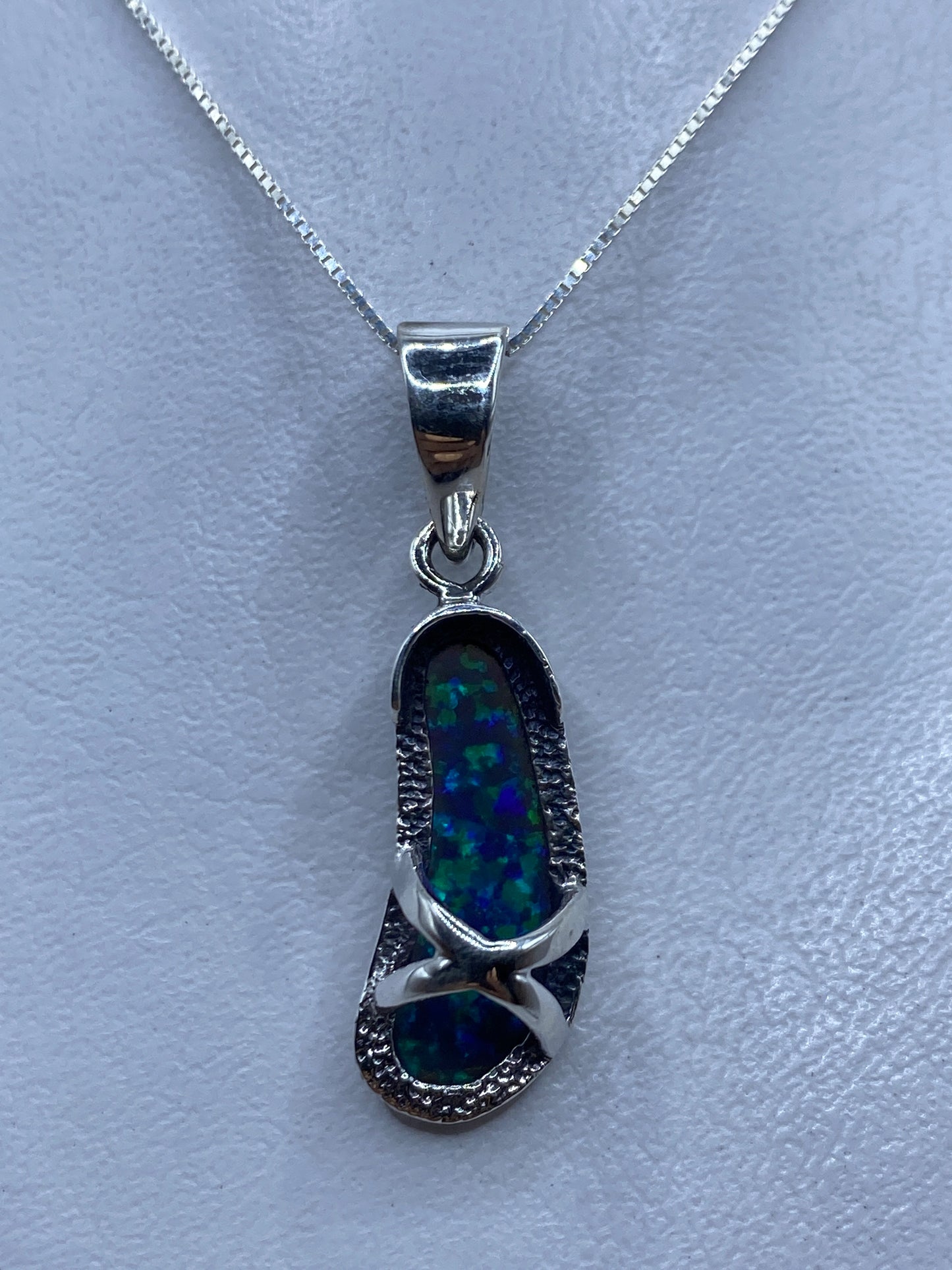 Dije de plata con ópalo de fuego azul, colgando de cadena plateada sobre fondo claro