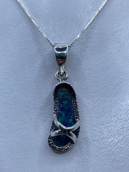Dije de plata con ópalo de fuego azul, colgando de cadena plateada sobre fondo claro