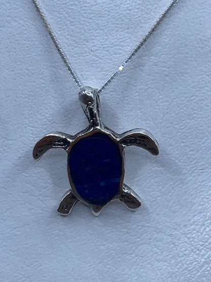 Dije tortuga en plata .925 con piedra azul engastada, colgando de cadena de plata fina
