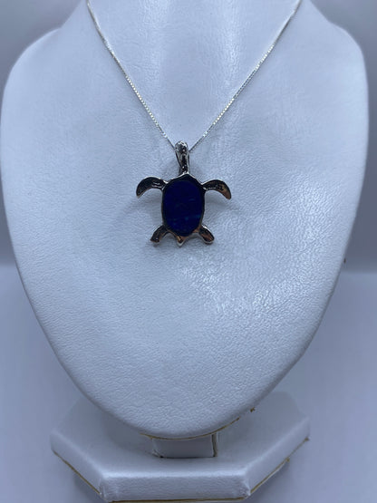 Detalle frontal del dije tortuga mostrando la piedra azul en el caparazón