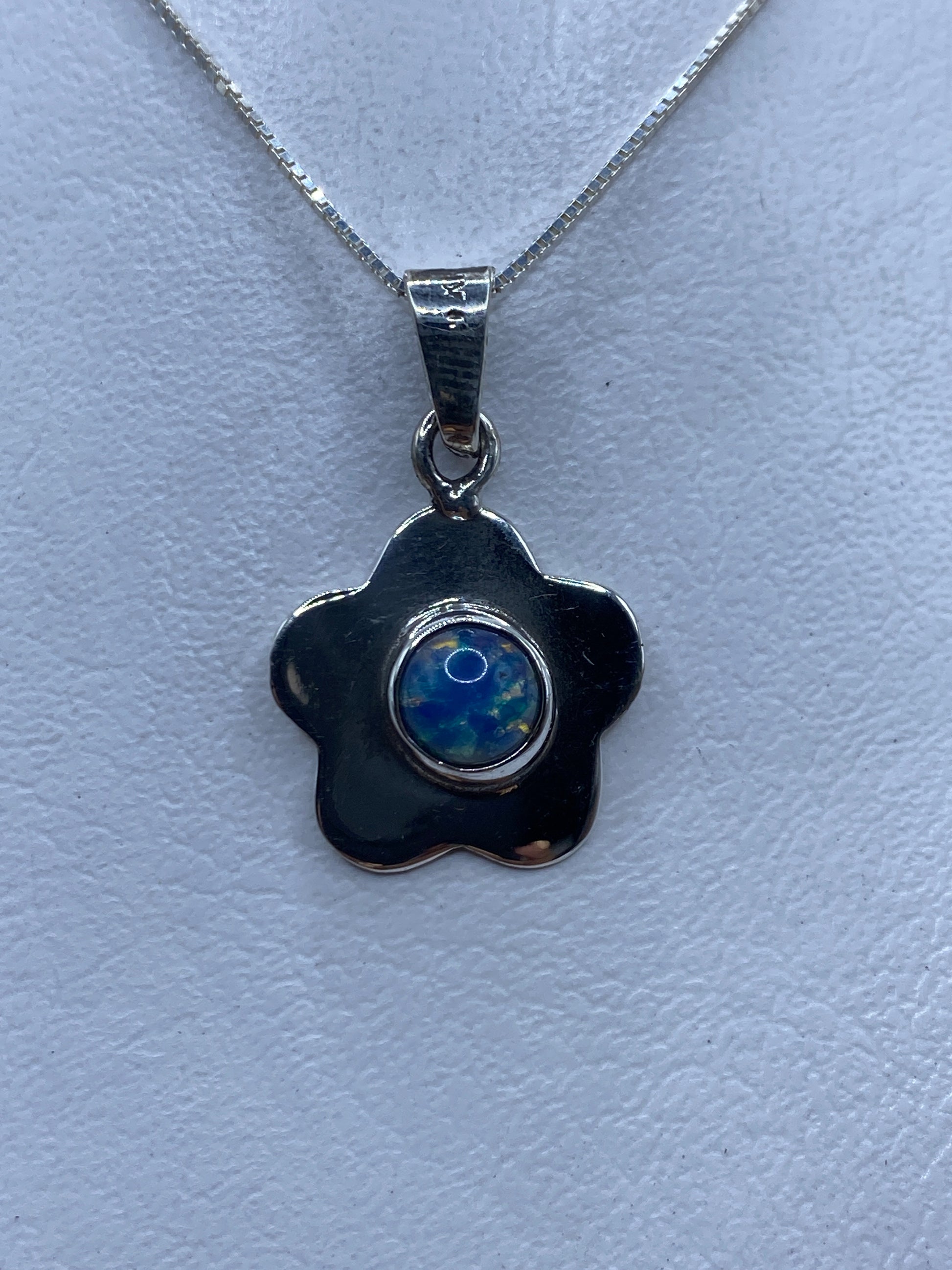 Dije floral de plata .925 con piedra multicolor azul y amarilla, colgado de una cadena plateada