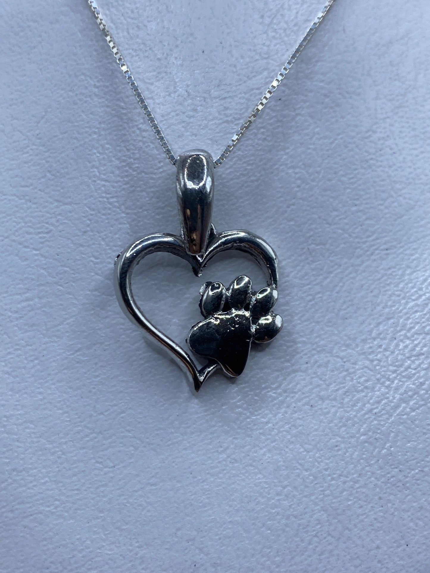 Dije de plata .925 en forma de corazón con pata, técnica de calado, sobre fondo blanco