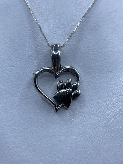 Dije de plata .925 en forma de corazón con pata, técnica de calado, sobre fondo blanco