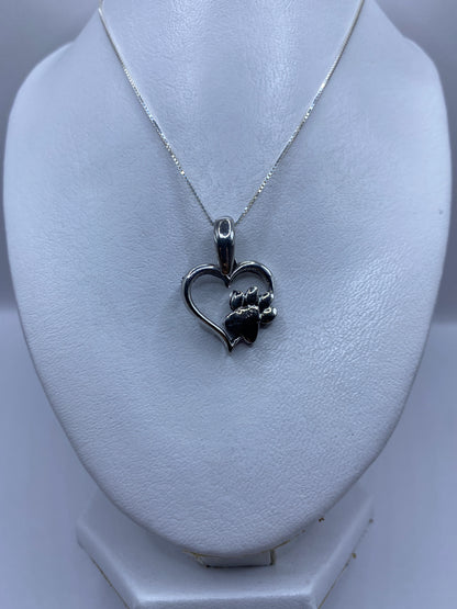 Vista frontal del dije de plata corazón y pata colgando de una cadena de plata delgada