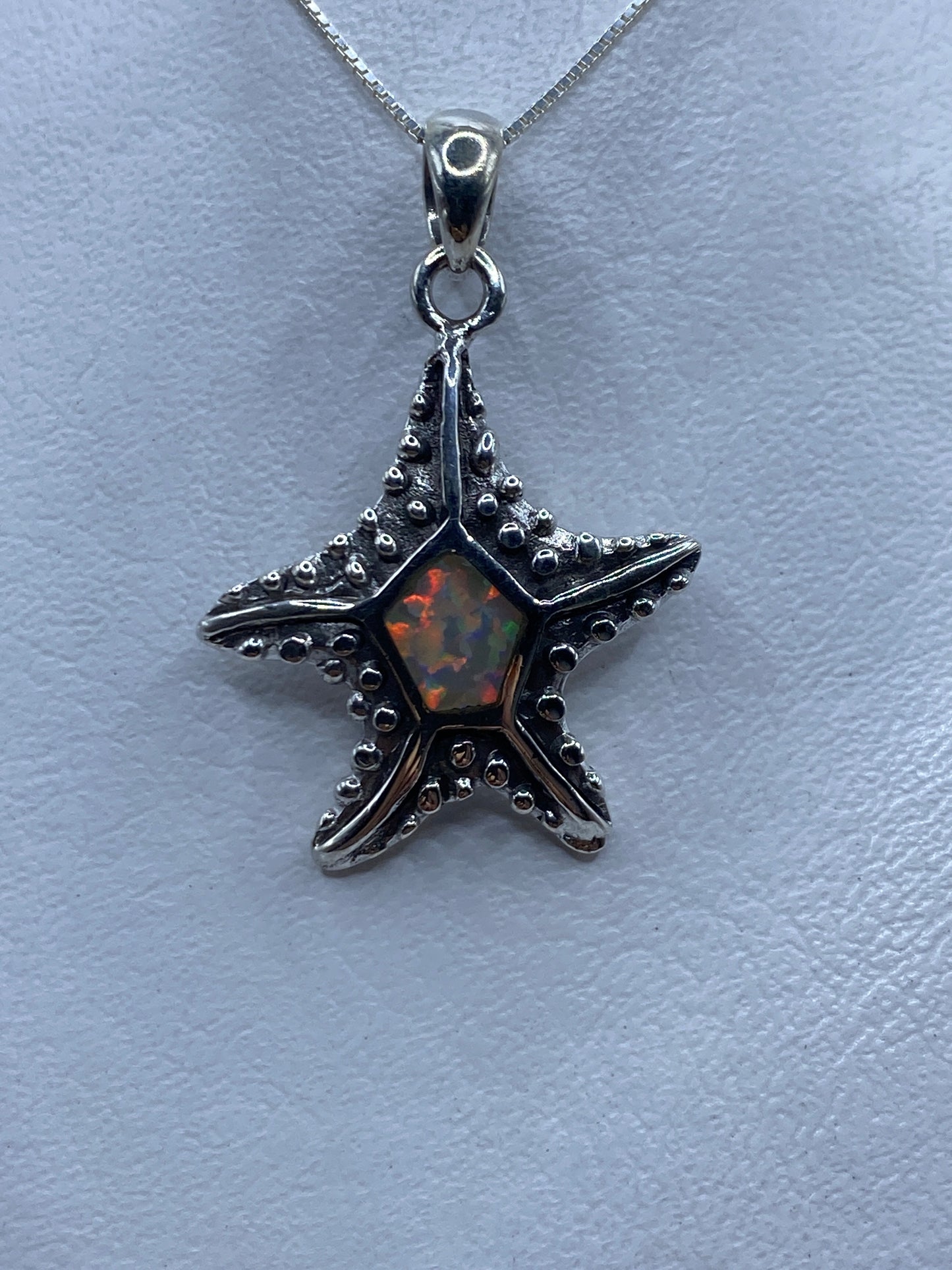 Dije estrella de plata .950 con ópalo de fuego naranja y rojo en el centro, sobre fondo azul claro