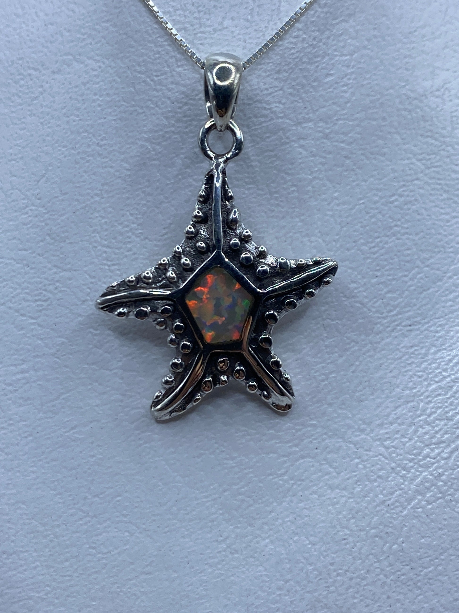 Dije estrella de plata .950 con ópalo de fuego naranja y rojo en el centro, sobre fondo azul claro