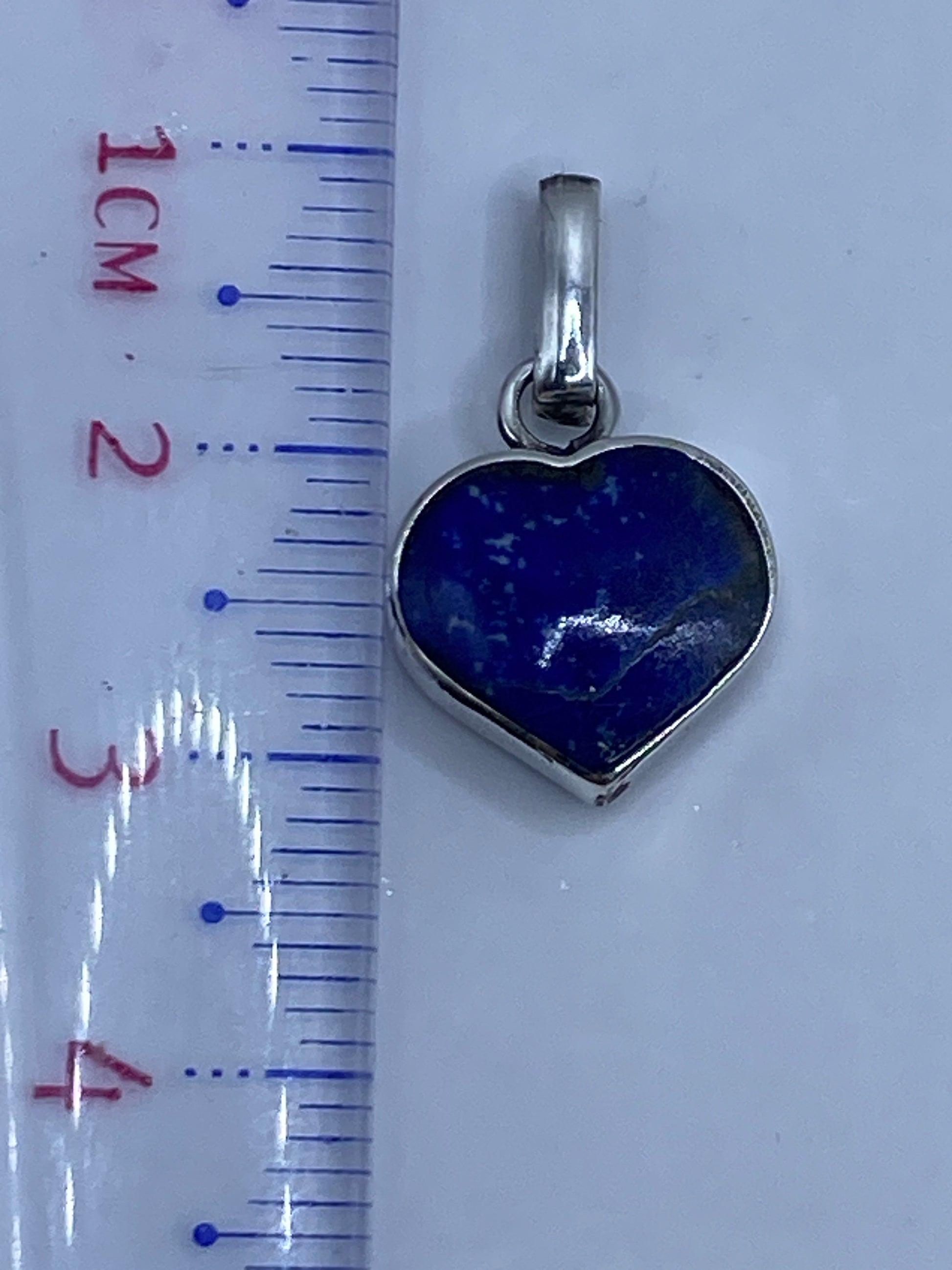 Dije de malaquita sobre regla métrica mostrando largo de 3.1 cm, con peso de 1.9 g en balanza