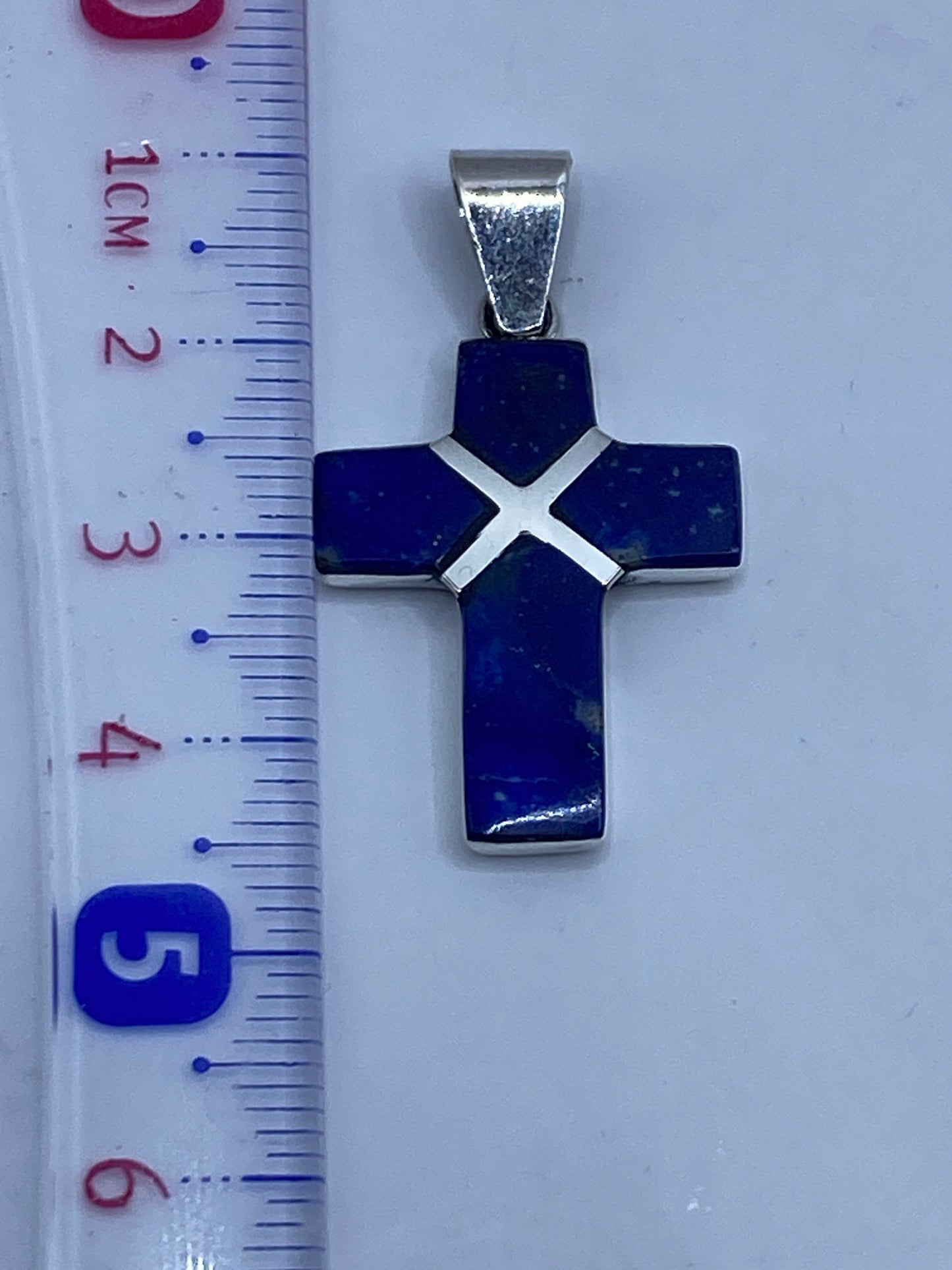 Dije cruz de plata .950 sobre superficie neutral, con hallmark .950 visible en el reverso