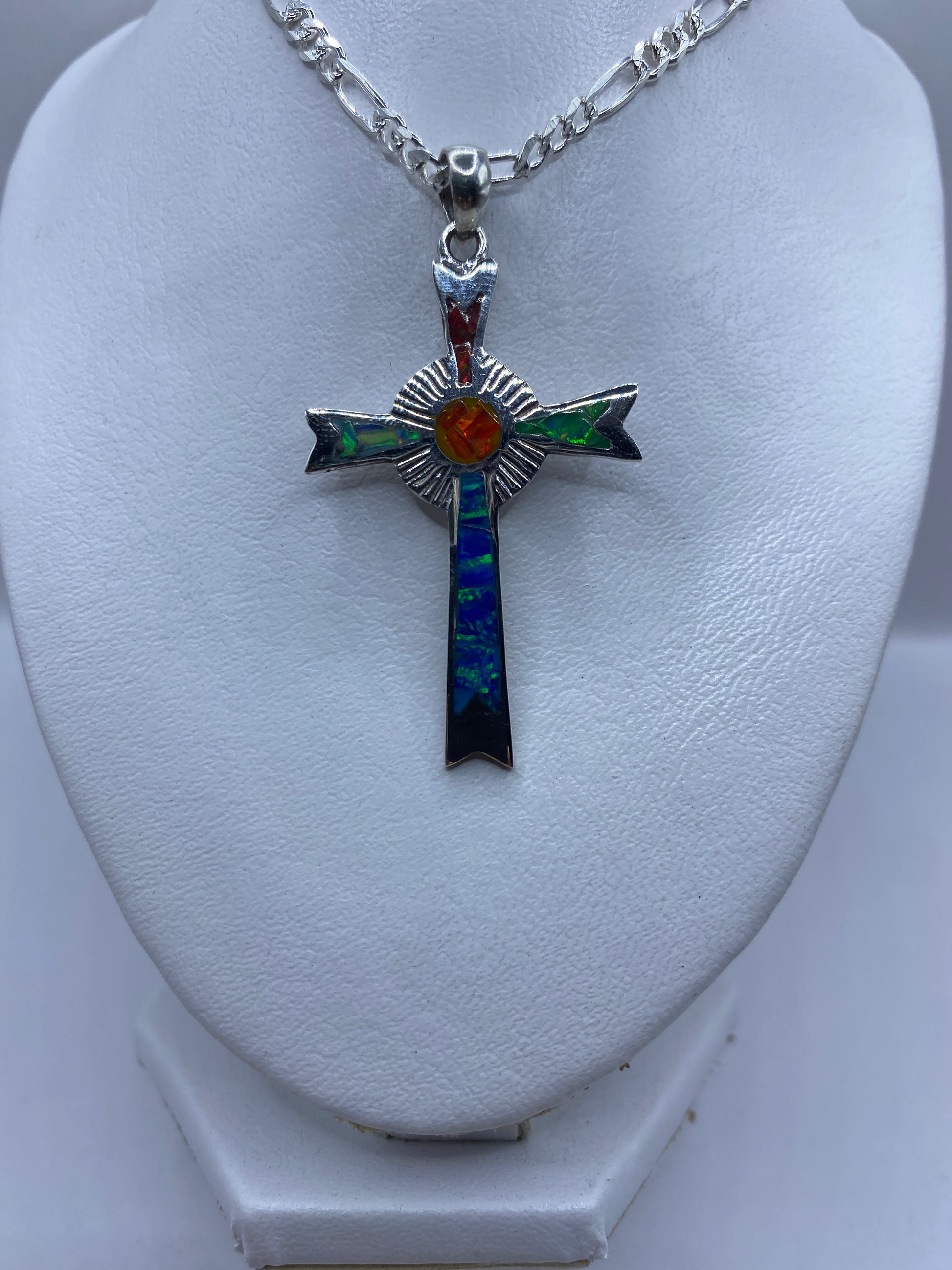 Cruz religiosa de plata con piedra ópalo que brilla en tonos rojos, verdes y azules