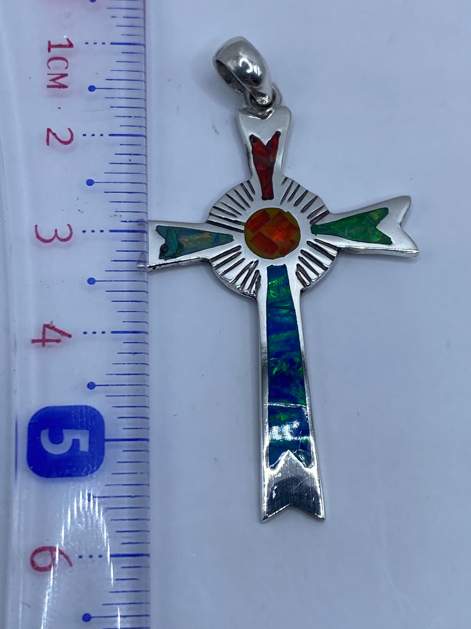 Dije cruz de plata sobre fondo blanco mostrando el Quinto .950 grabado en la parte trasera