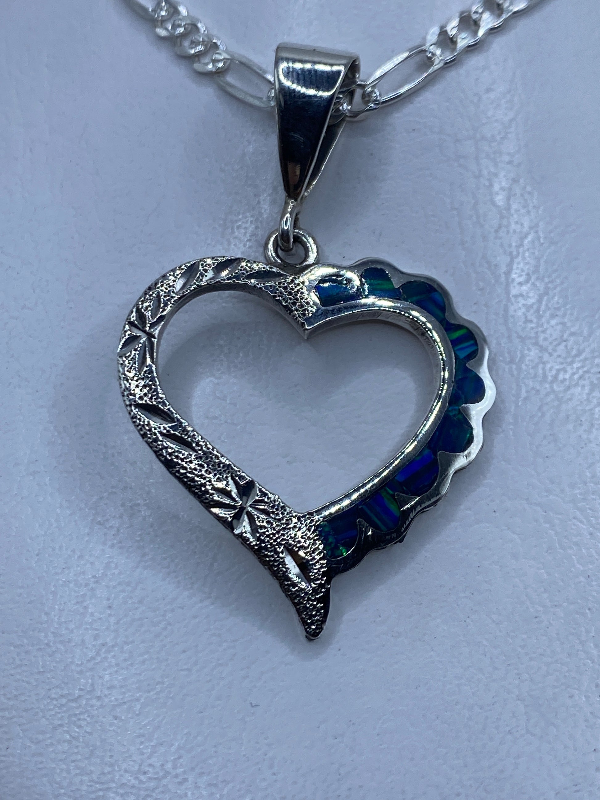 Dije de plata corazón con ópalo de fuego azul profundo, colgante sobre fondo blanco