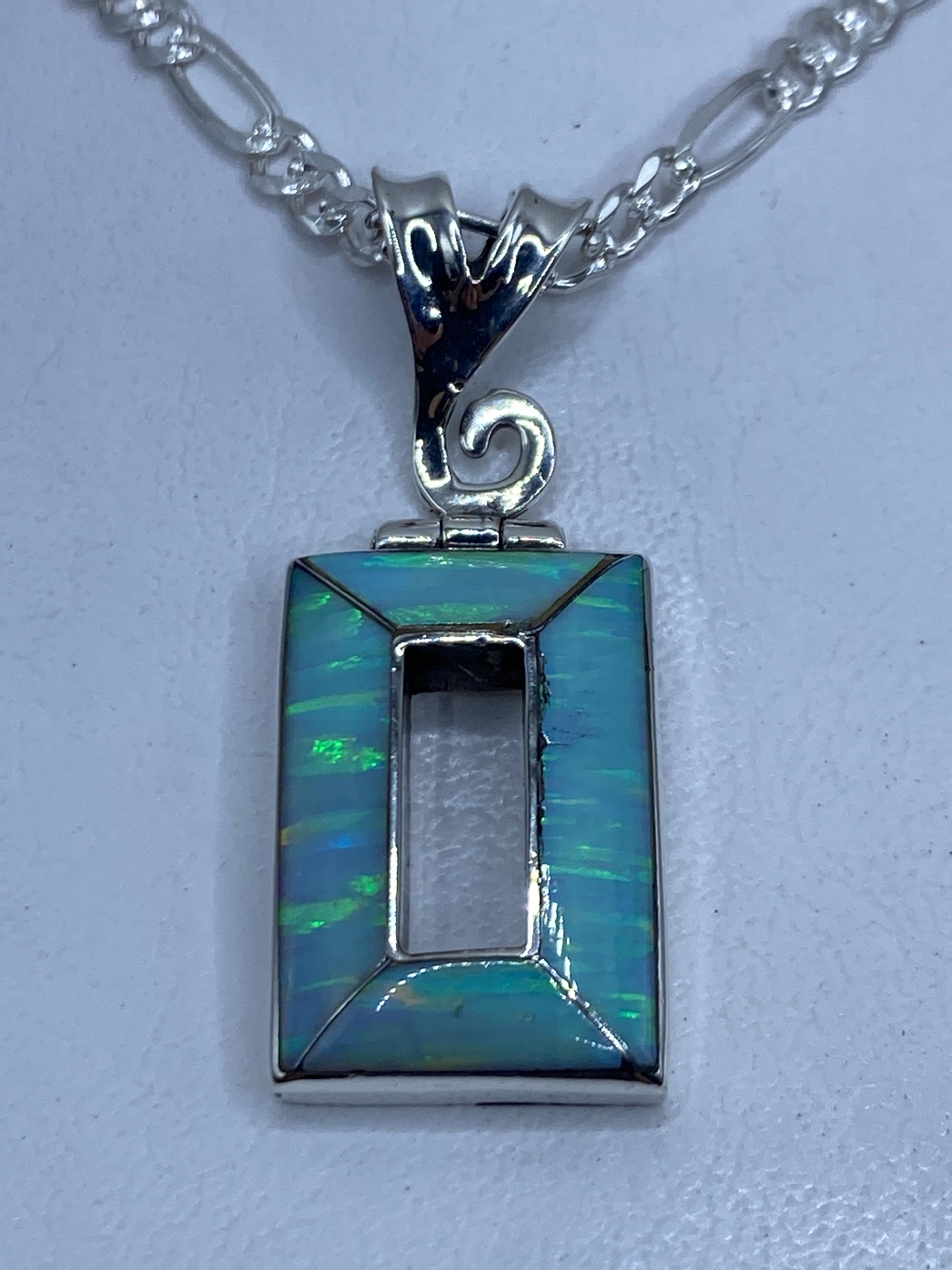 Dije rectangular de plata .950 con ópalo de fuego azul cielo, colgando de una cadena Figaro