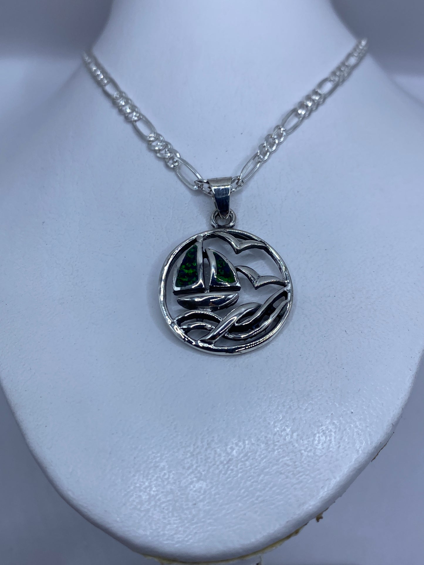 Primer plano del dije de plata mostrando el relieve del velero y la vela con ópalo