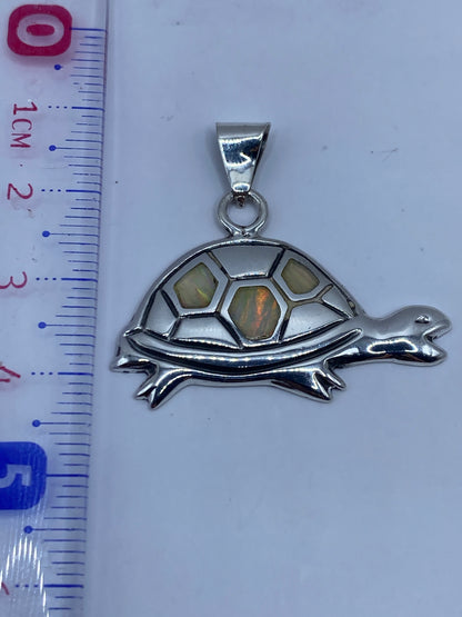Dije de tortuga de 3.5 cm de largo sobre fondo blanco mostrando el acabado pulido