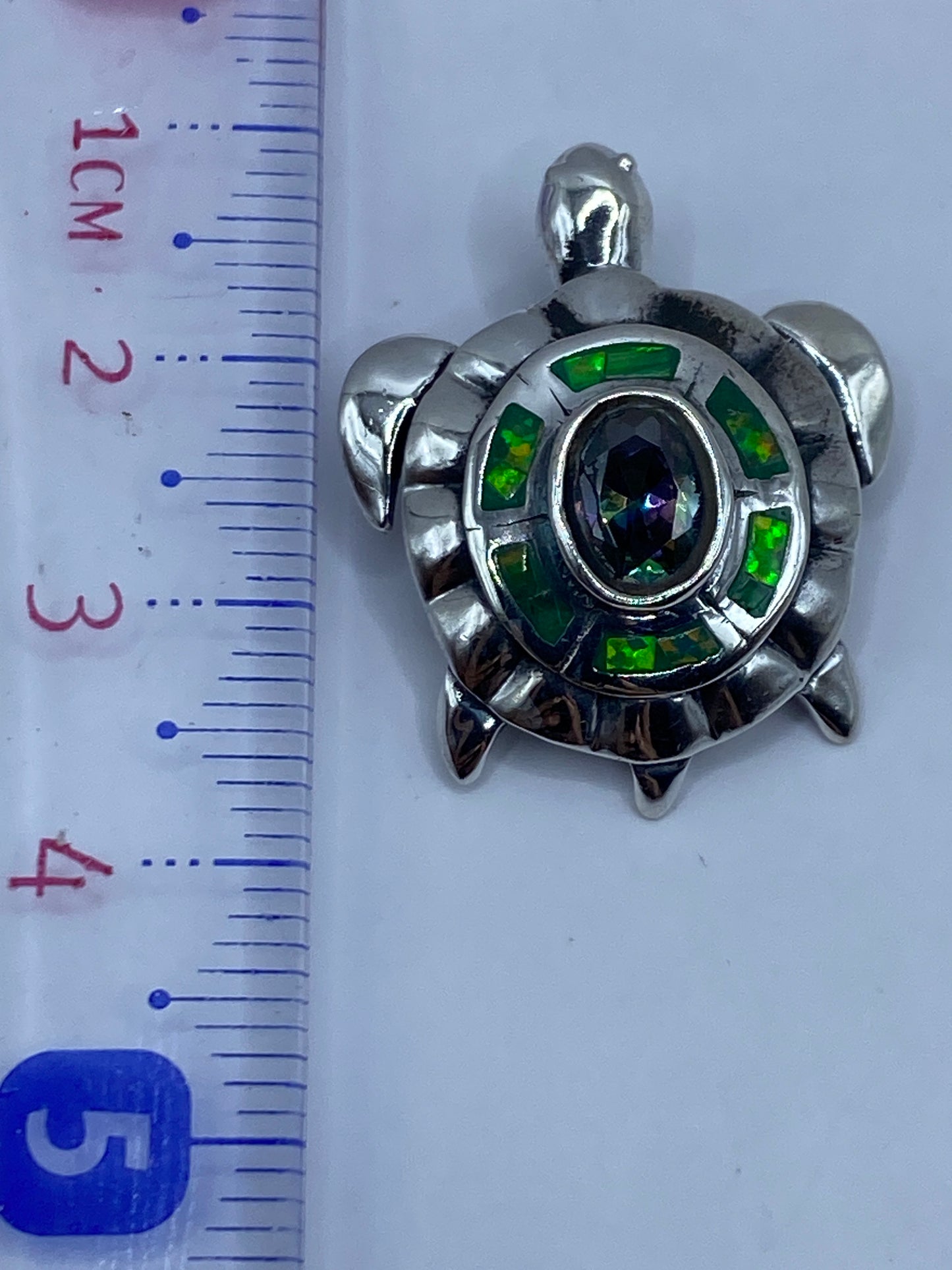 Dije tortuga junto a regla de centímetros, mostrando tamaño real de 3.3 cm
