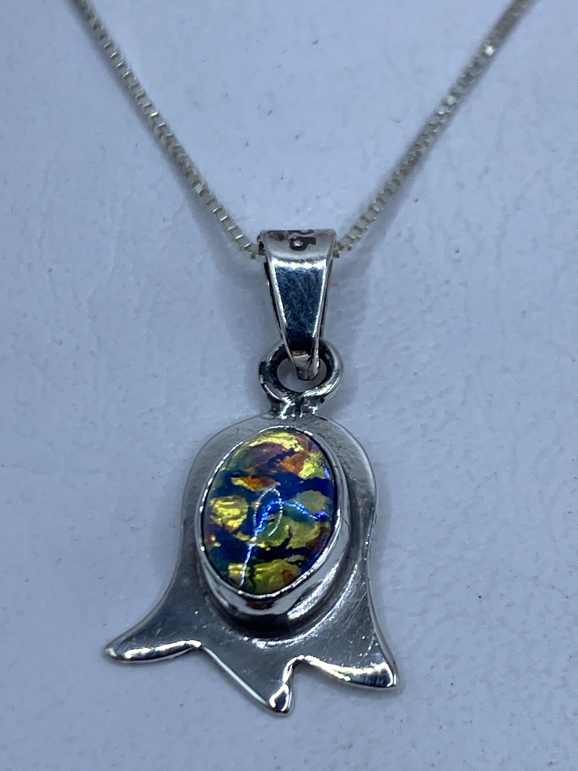 Dije de plata en forma de campana con piedras multicolor, colgado de cadena plateada