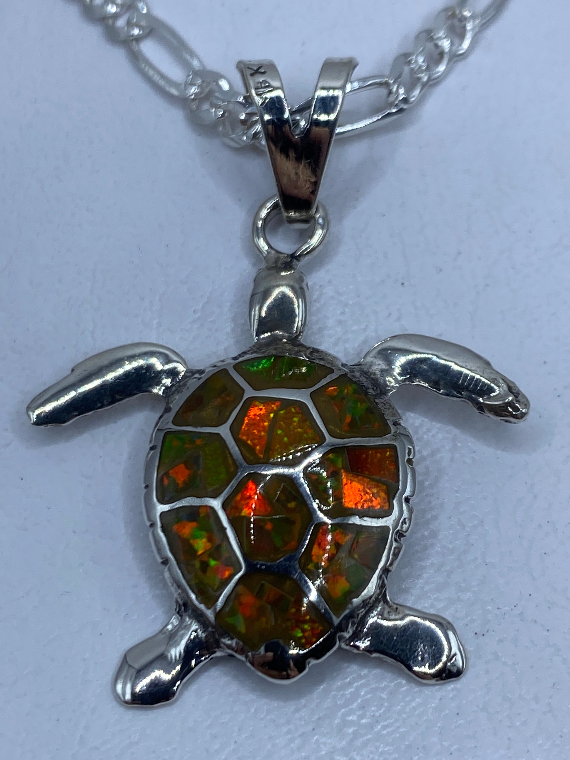 Dije tortuga de plata .950 con ópalo de fuego amarillo incrustado, colgando de una cadena Figaro pulida