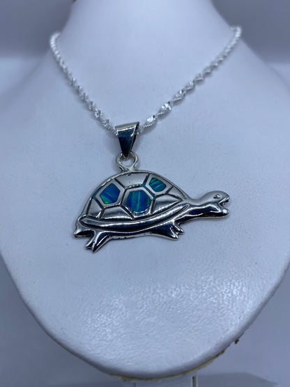 Dije de tortuga de frente, mostrando el diseño completo y los tonos azules de la piedra