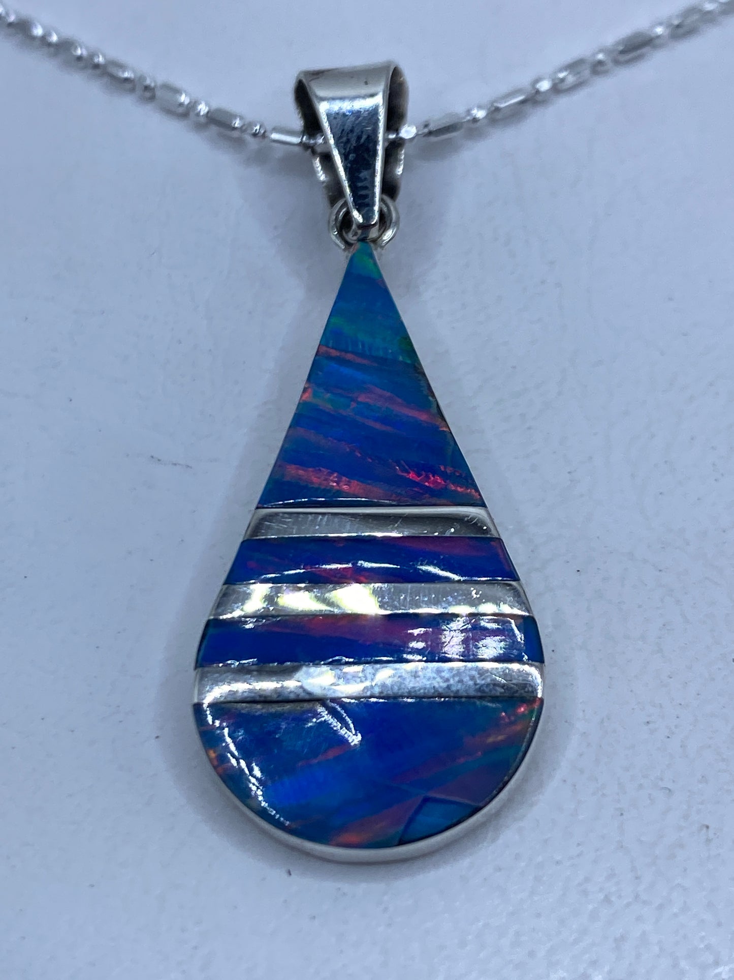 Dije de plata en forma de gota con ópalo de fuego azul engastado, colgando de una cadena de eslabones