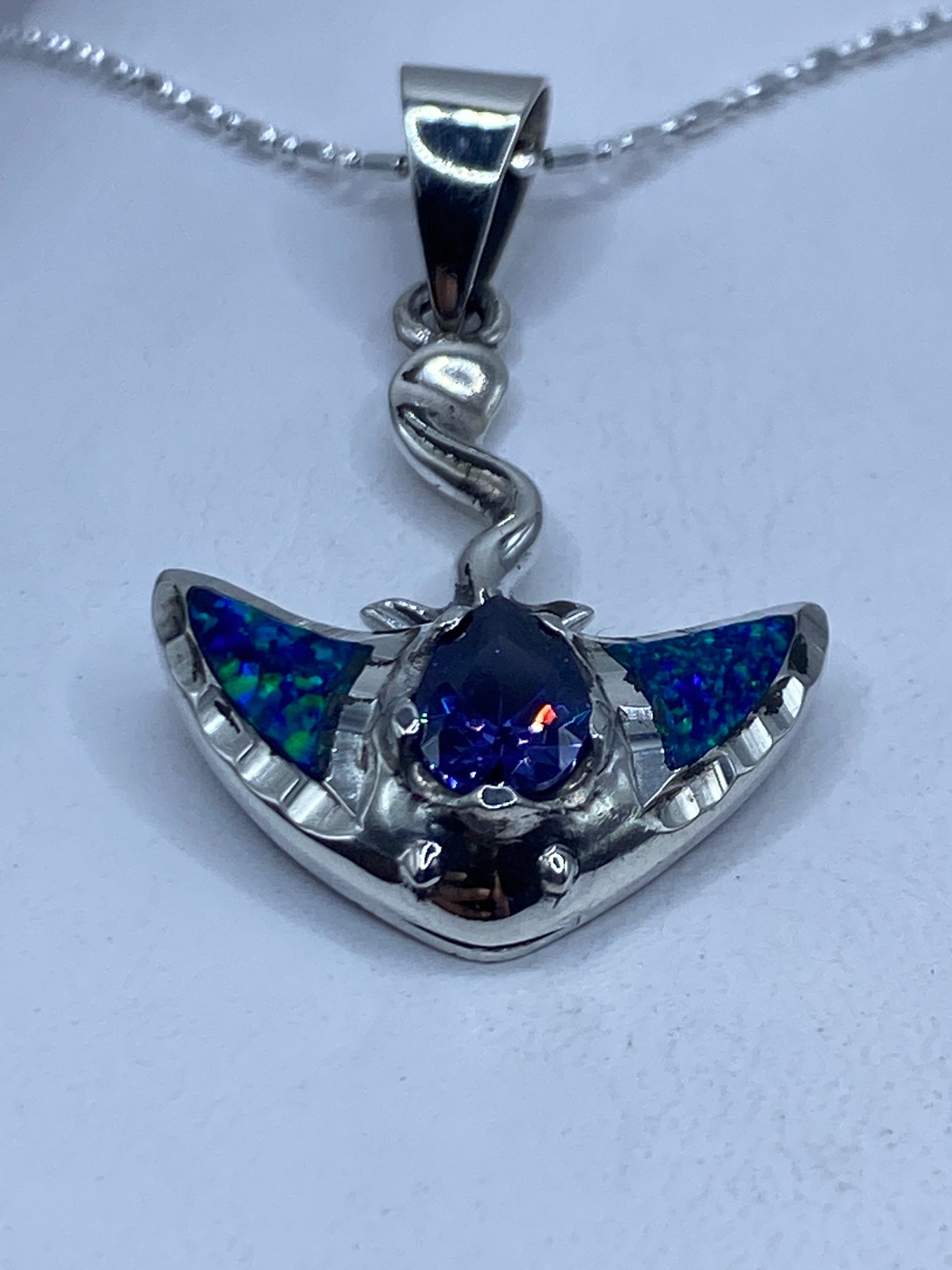 Dije de plata .950 con ópal de fuego azul engastado, suspendido en cadena de plata sobre pecho blanco