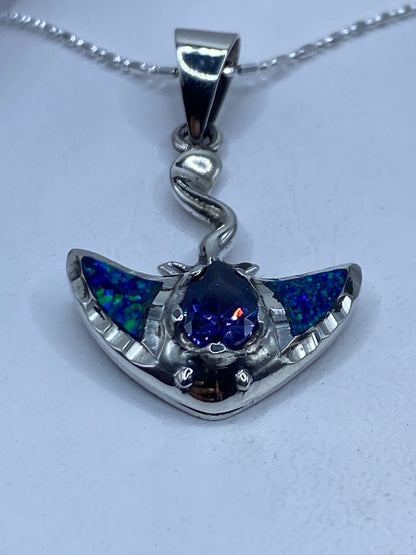 Dije de plata .950 con ópal de fuego azul engastado, suspendido en cadena de plata sobre pecho blanco