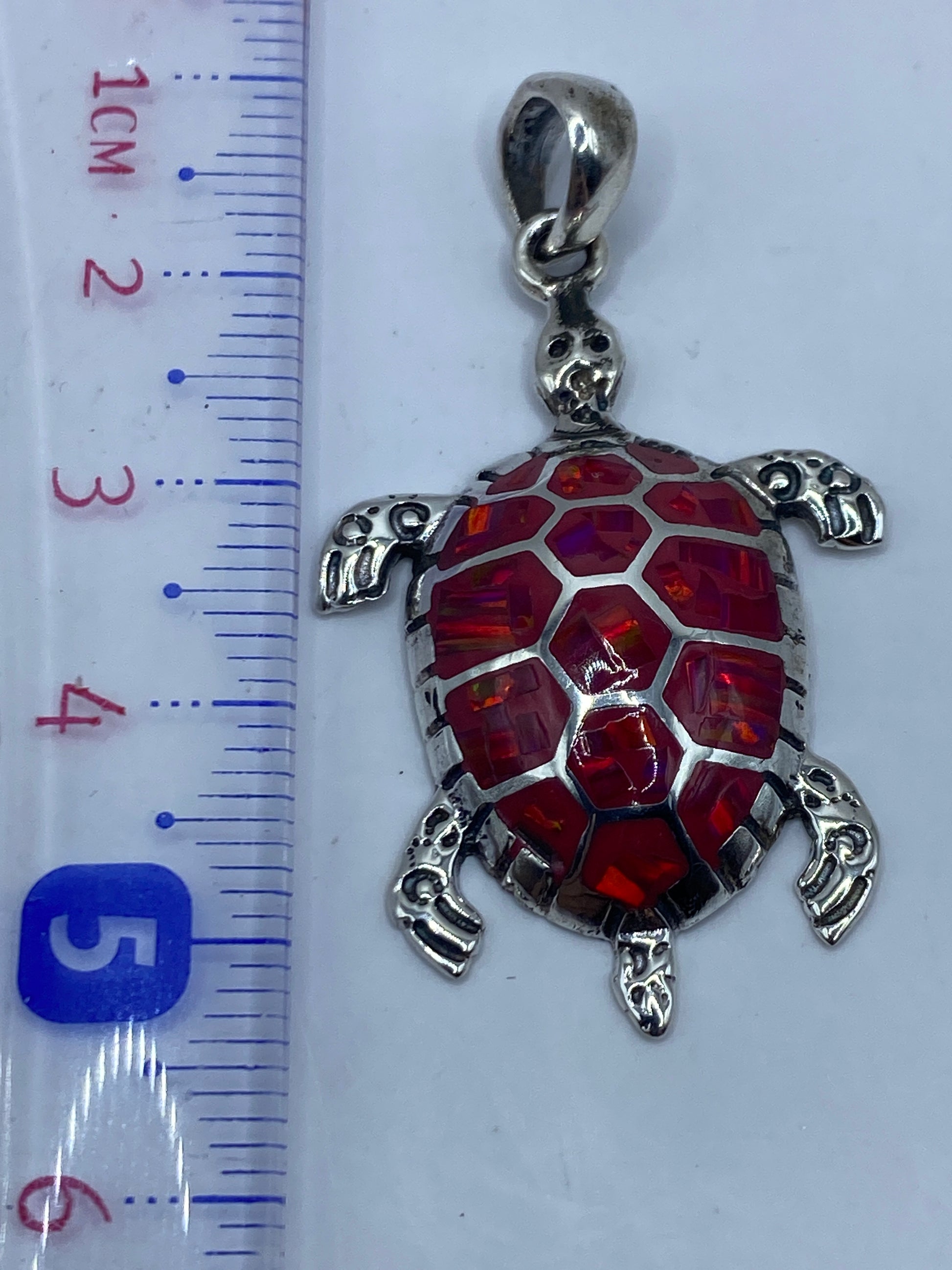 Dije de tortuga sobre escala mostrando 5.2 cm de largo, sin cadena