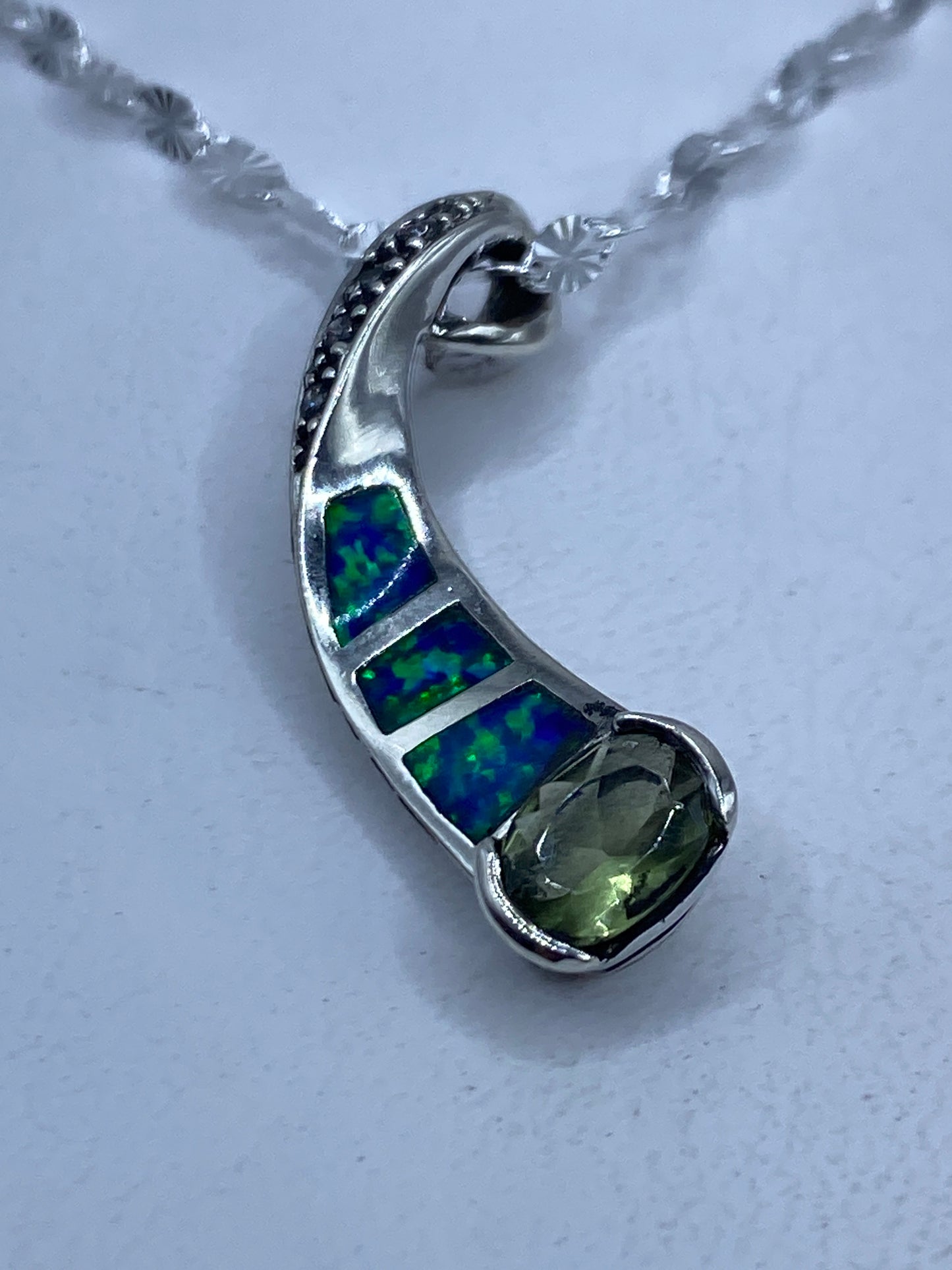 Dije de plata .925 con ópalo de fuego engastado, tonos azul verdoso, colgando de cadena de plata