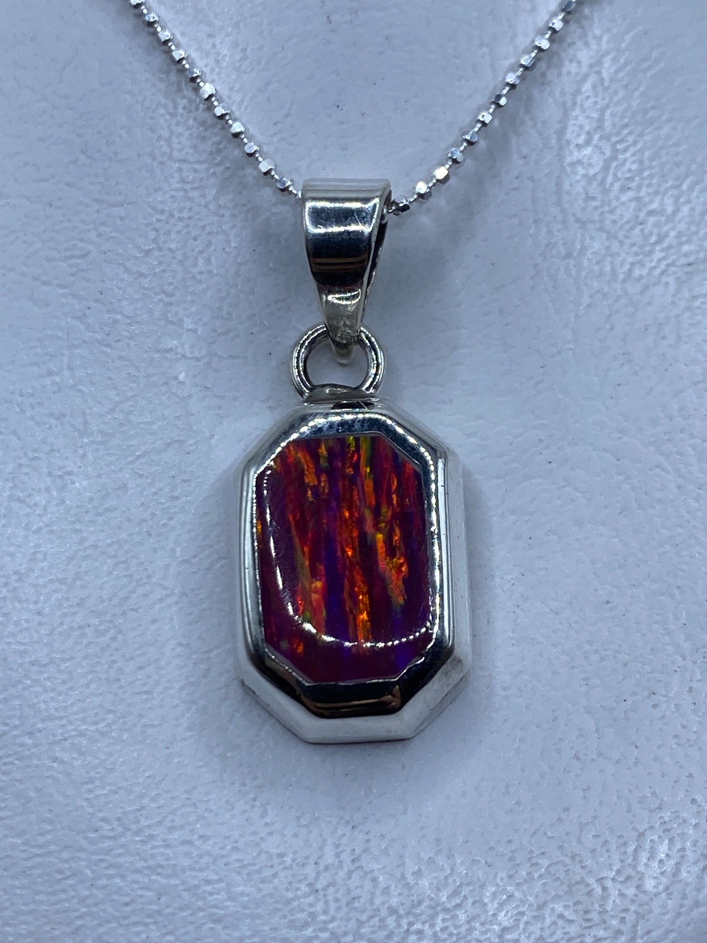 Dije de plata .950 con Opalo de Fuego rosa engastado, sobre fondo blanco, mostrando el brillo luminoso de la piedra