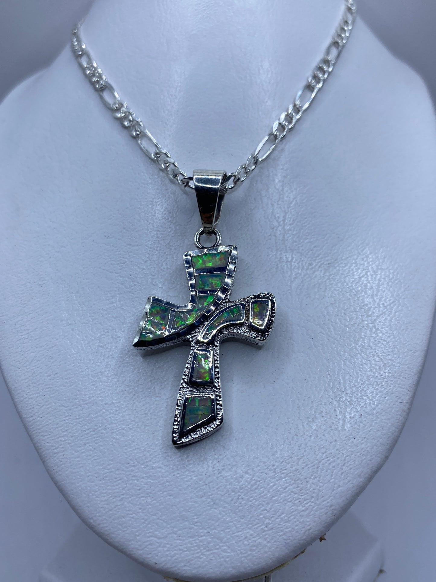 Detalle frontal de la cruz de plata mostrando los esmaltes de ópalo de fuego verde y naranja
