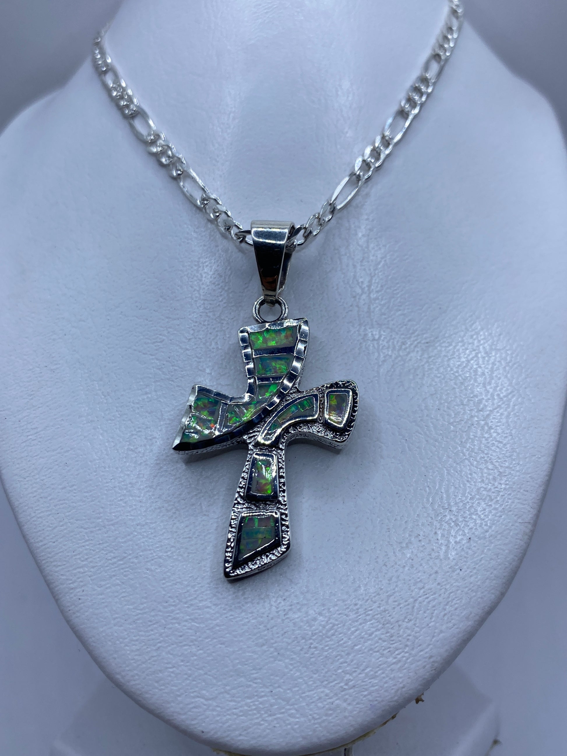 Detalle frontal de la cruz de plata mostrando los esmaltes de ópalo de fuego verde y naranja