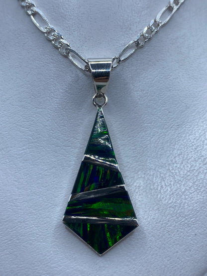 Dije tetraédrico de plata .950 con ópalo de fuego verde sobre cadena figaro en la piel