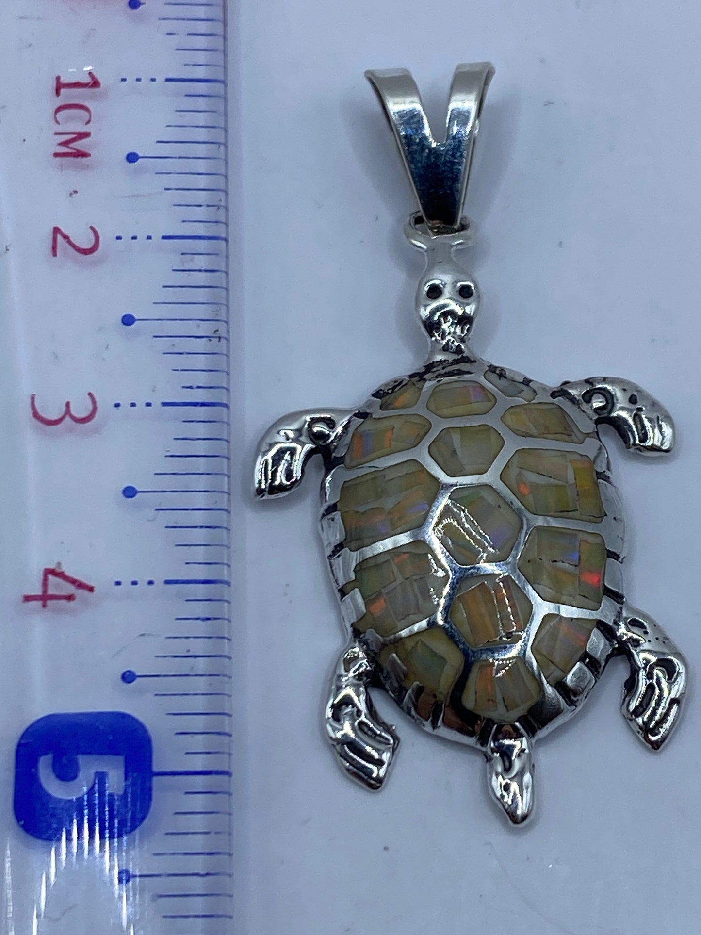 Dije de tortuga de 5.1 cm sobre regla de medida, mostrando tamaño real junto a Quinto .950