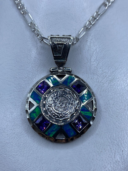 Dije circular de plata .950 con opalo de fuego azul y relieve prehispanico, colgando de cadena
