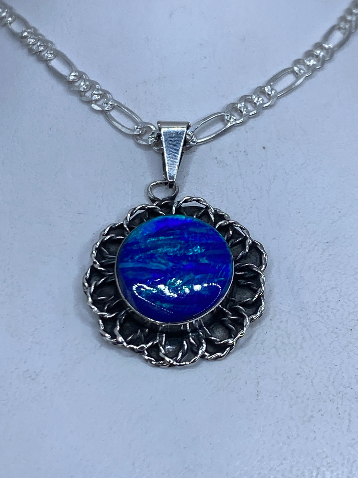 Dije de plata con Ópalo de Fuego azul profundo en marco floral grabado, sobre cadena figaro