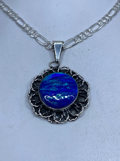 Dije de plata con Ópalo de Fuego azul profundo en marco floral grabado, sobre cadena figaro