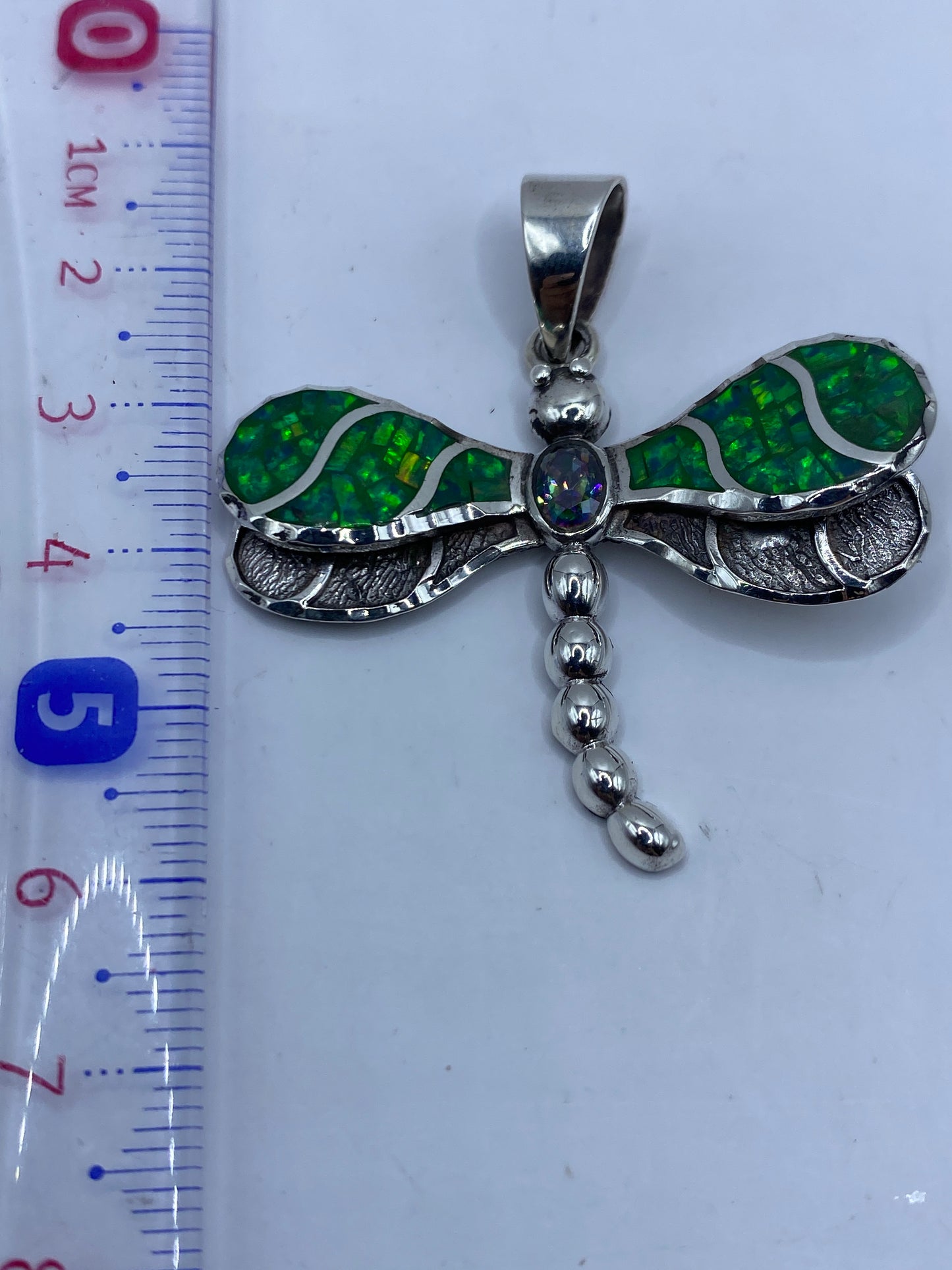 Dije libélula junto a regla mostrando largo de 5.6 cm