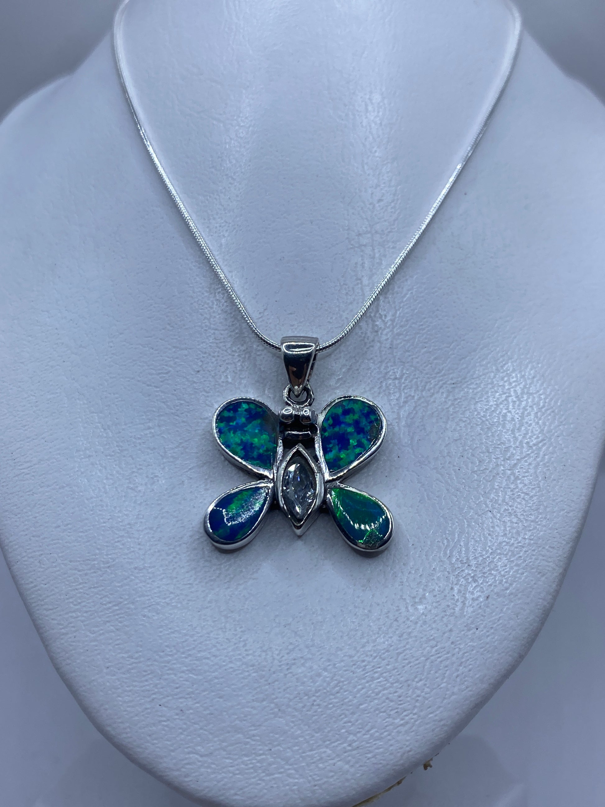 Detalle del dije mariposa mostrando el juego de color azul y verde del ópalo de fuego