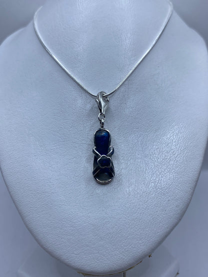Dije de 4.1 cm de largo con piedra azul en primer plano sobre pecho de mujer