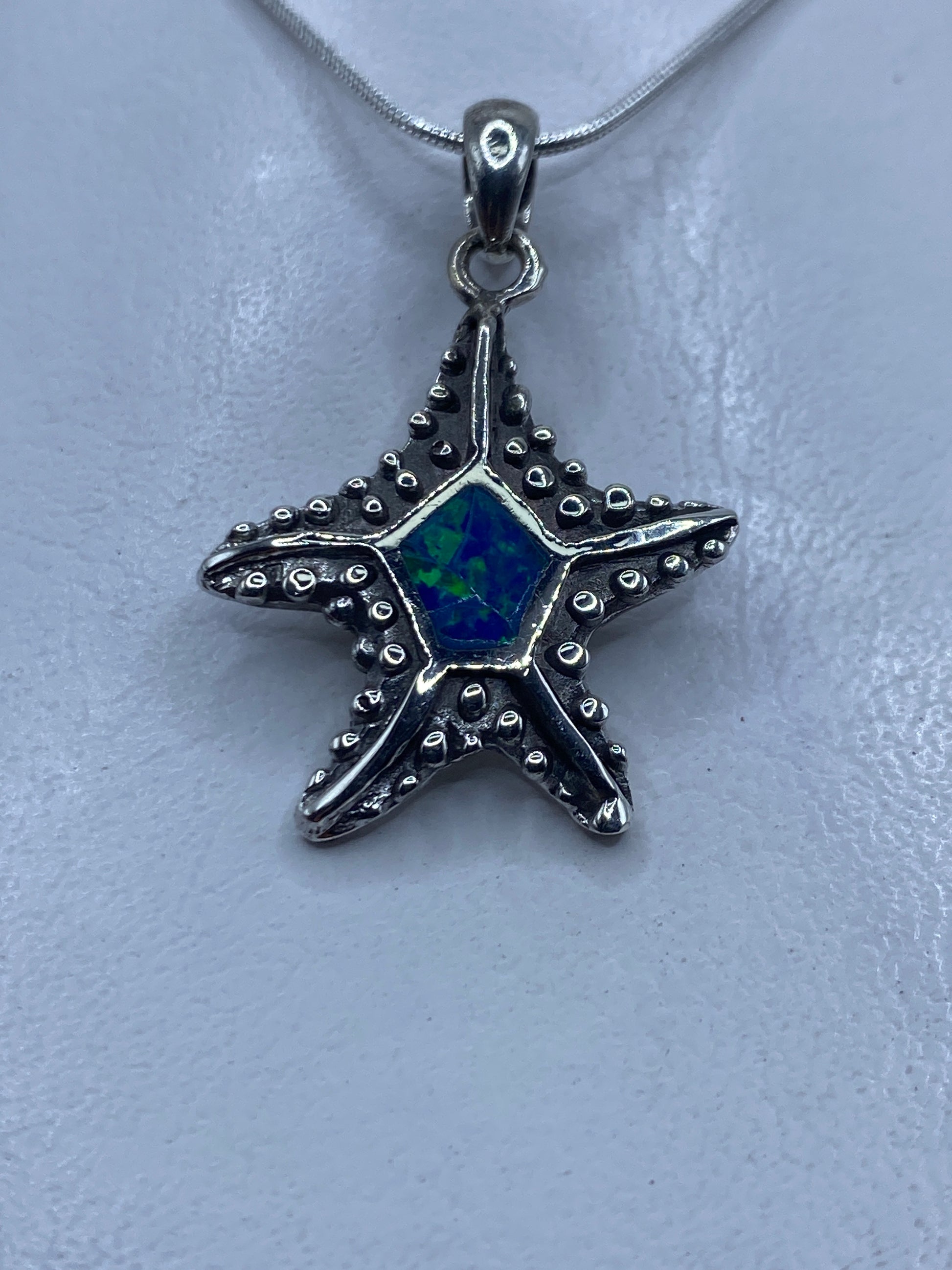 Dije de plata en forma de estrella marina con ópalo de fuego azul en el centro