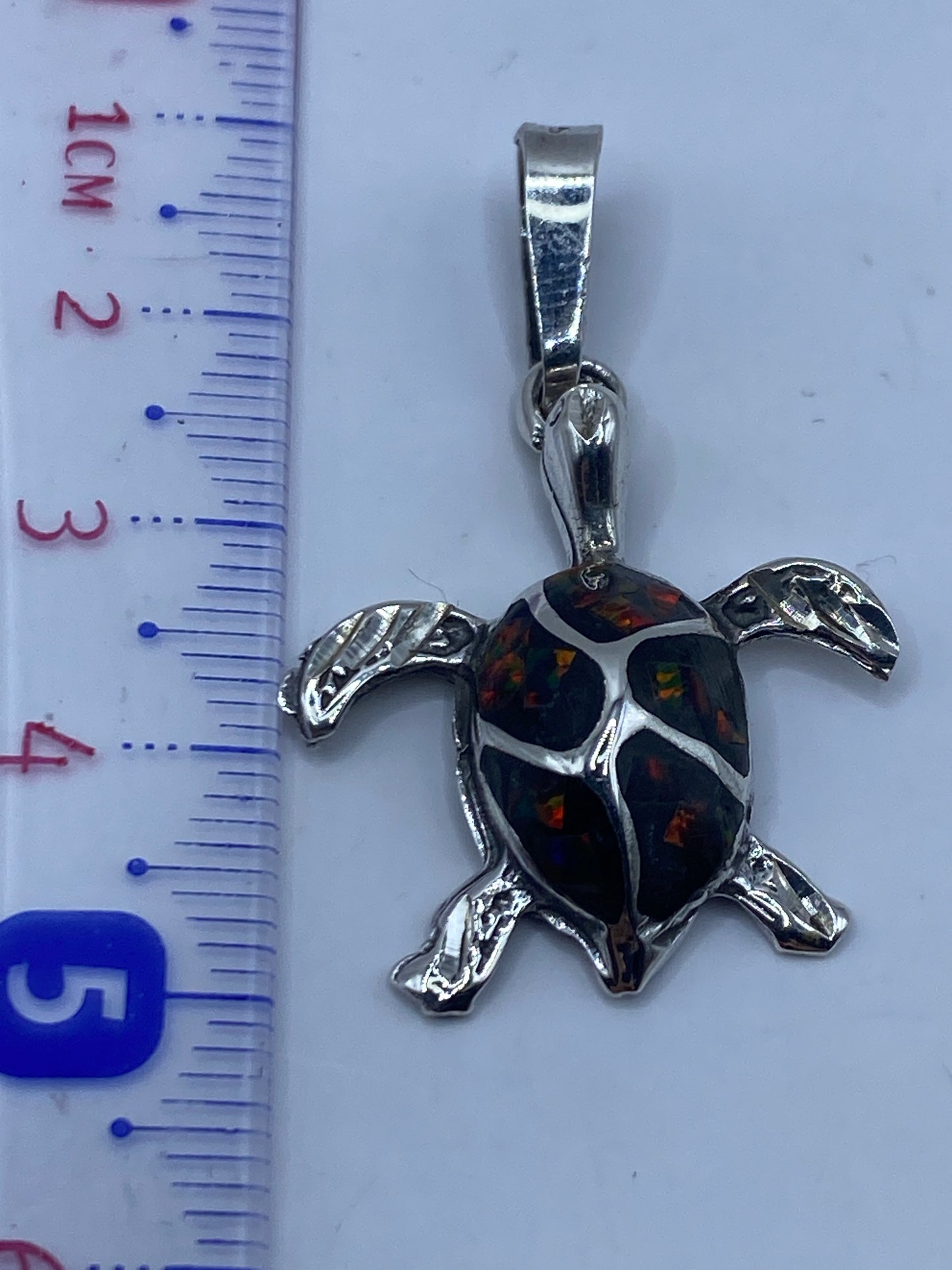 Dije tortuga sobre fondo blanco junto a regla, mostrando 4.7 cm de largo