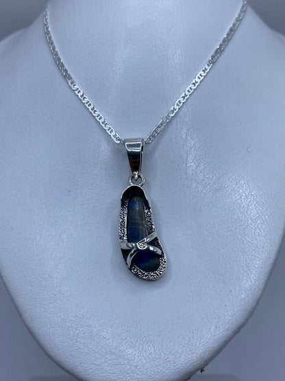 Dije de 4.5 cm sobre el pecho, mostrando el brillo azul del ópalo