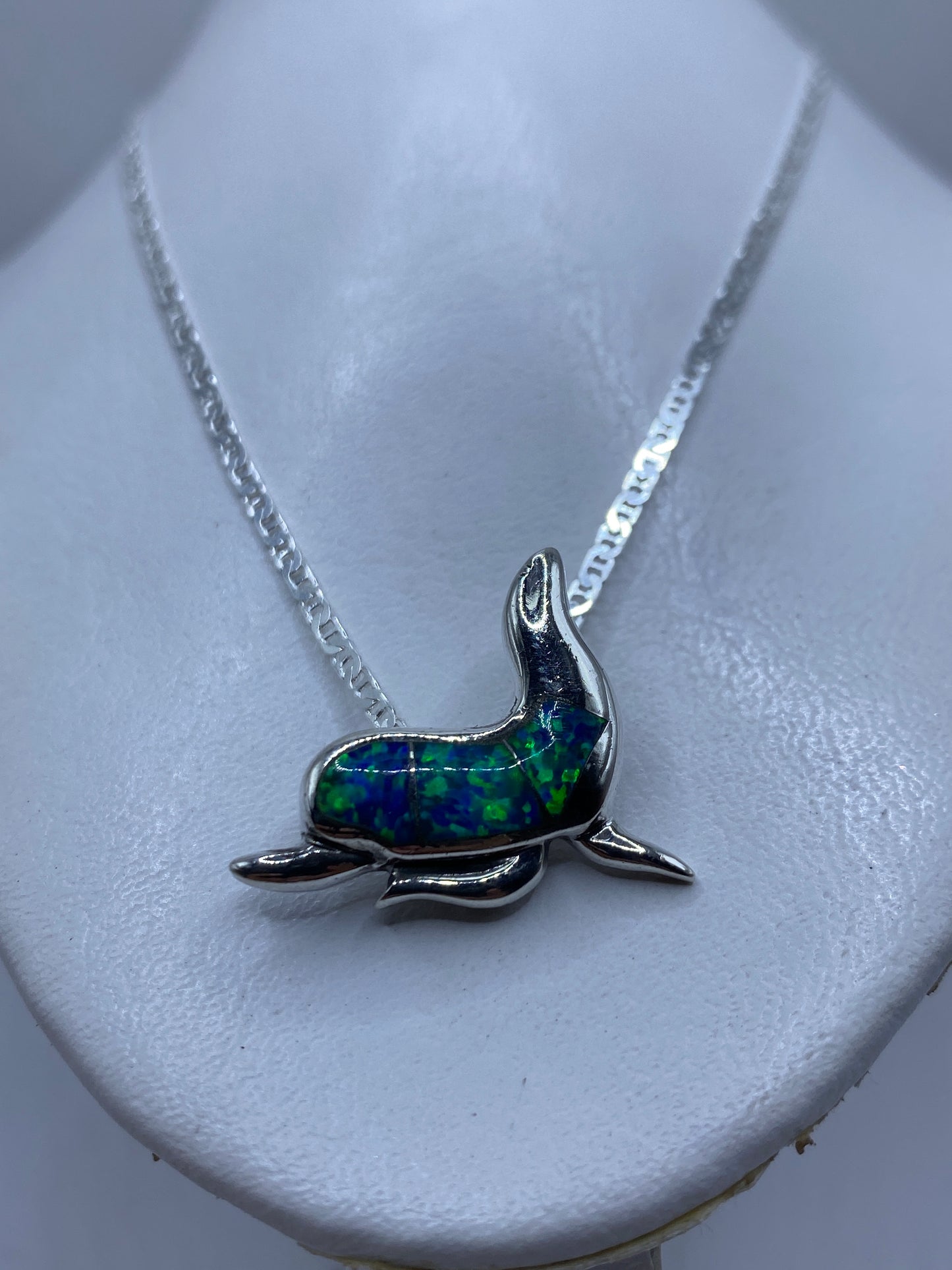 Dije de delfín puesto al cuello sobre piel, efecto del ópalo reflejando luz azul verdosa