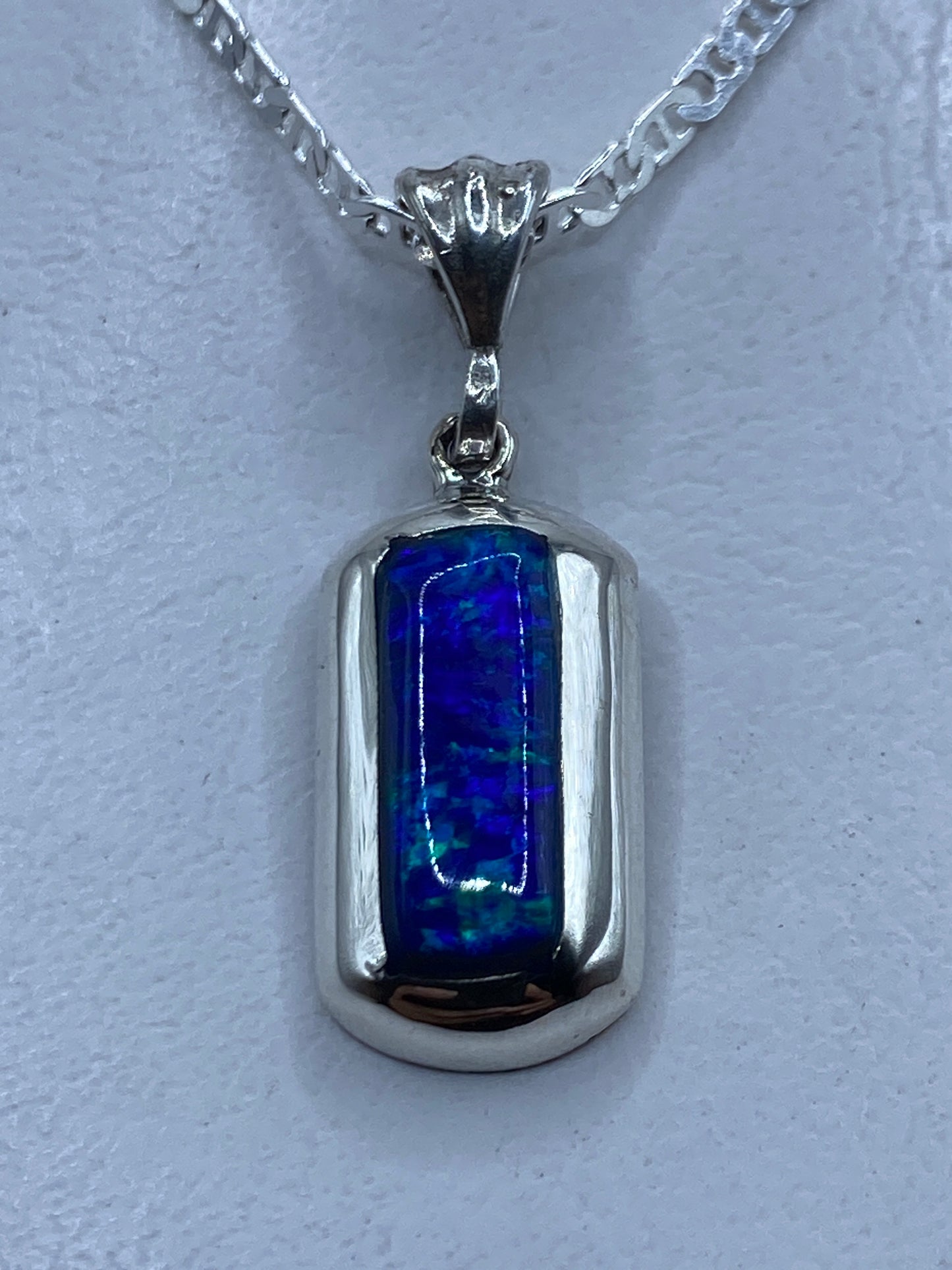 Dije de plata con ópalo de fuego azul colgando de cadena plateada