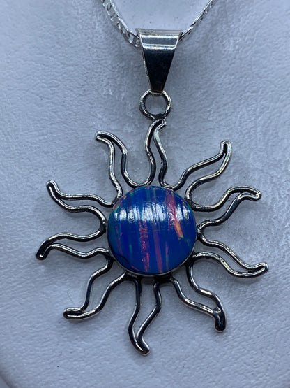 Dije sol de plata con ópalo de fuego azul, colgando en el pecho sobre un fondo blanco