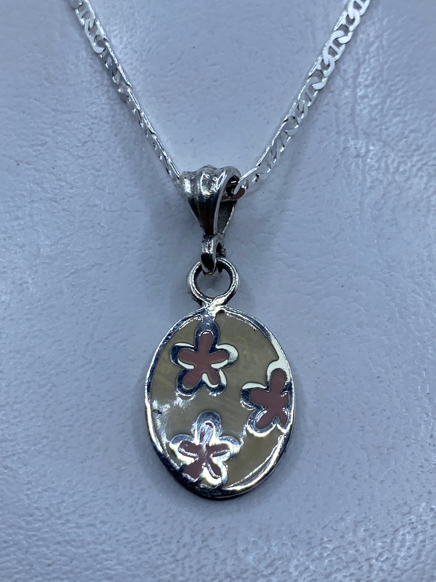 Dije de plata con flores en relieve, colgante en cadena plateada sobre fondo gris